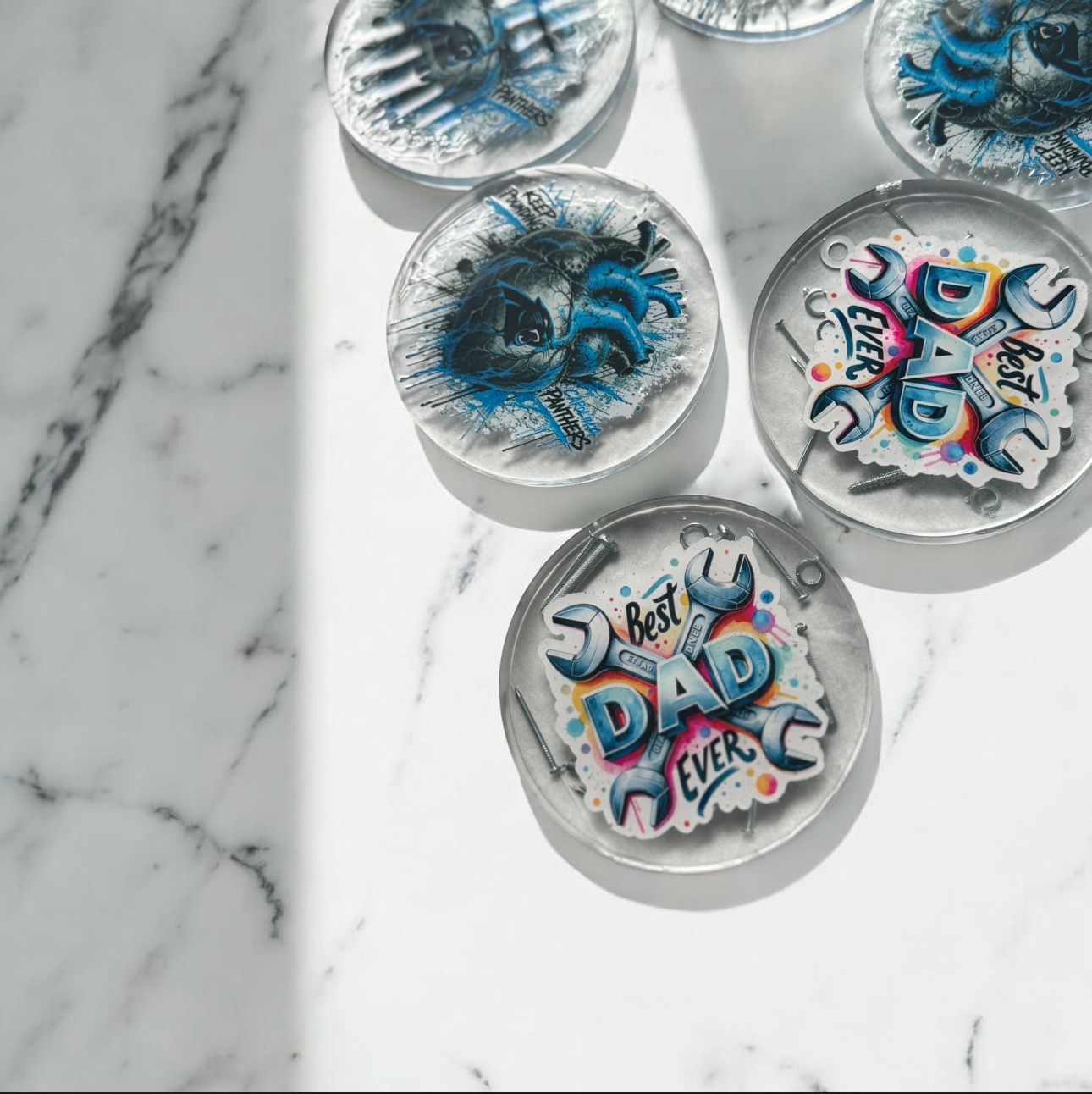 Square resin coasters featuring NC State and UNC Tarheels graffiti logos freshly poured in silicone molds on a teal silicone mat in the studio.